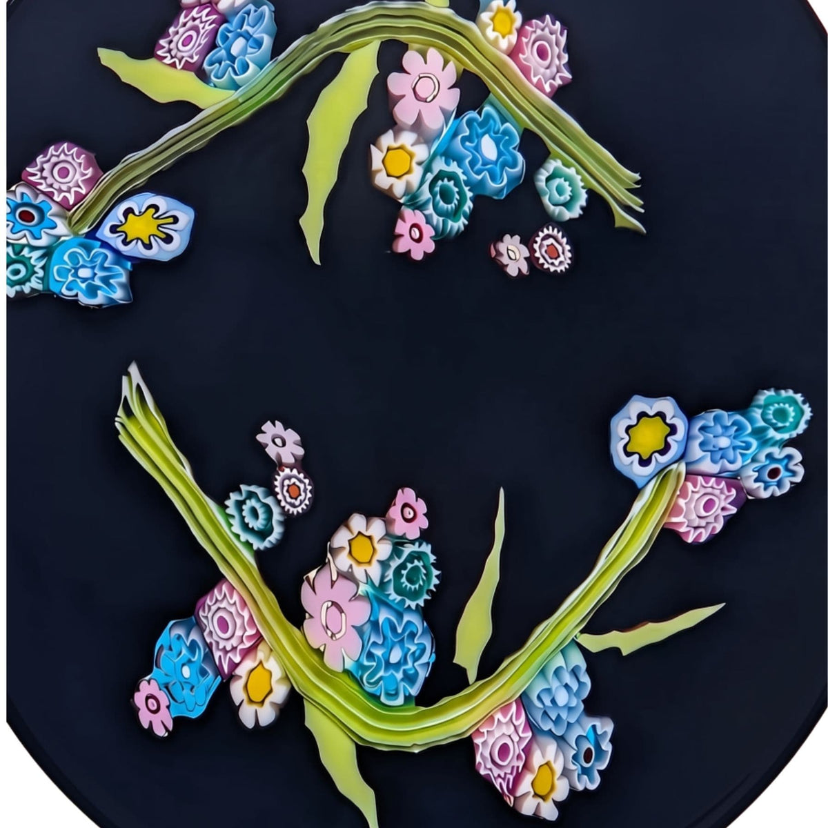 A circular black millefiori murano glass piece featuring two curved green stems decorated with colourful flowers in pink, blue, white, and yellow.