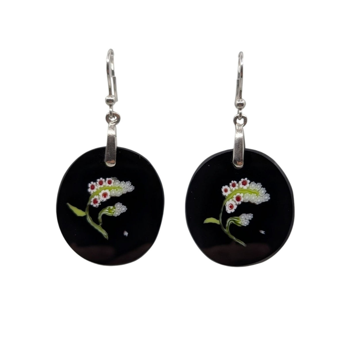 A pair of silver leverback earrings featuring round black glass pendants decorated with millefiori glass white lily of the valley flowers with green leaves and small red centers, shown against a plain white background.