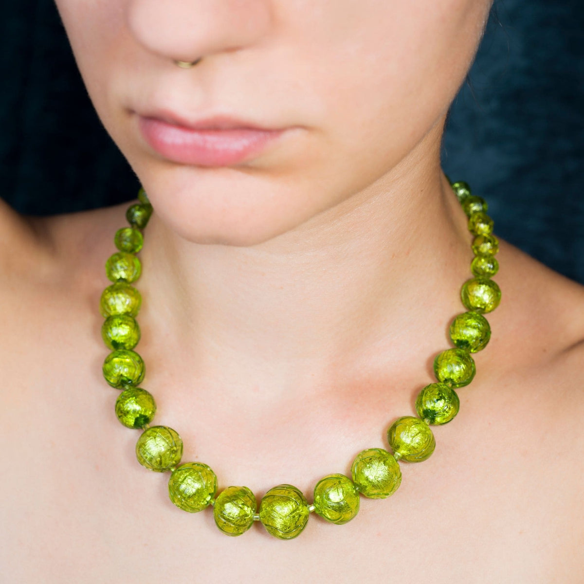 A close-up of a person wearing a chunky olive green beaded necklace with a textured, metallic finish.