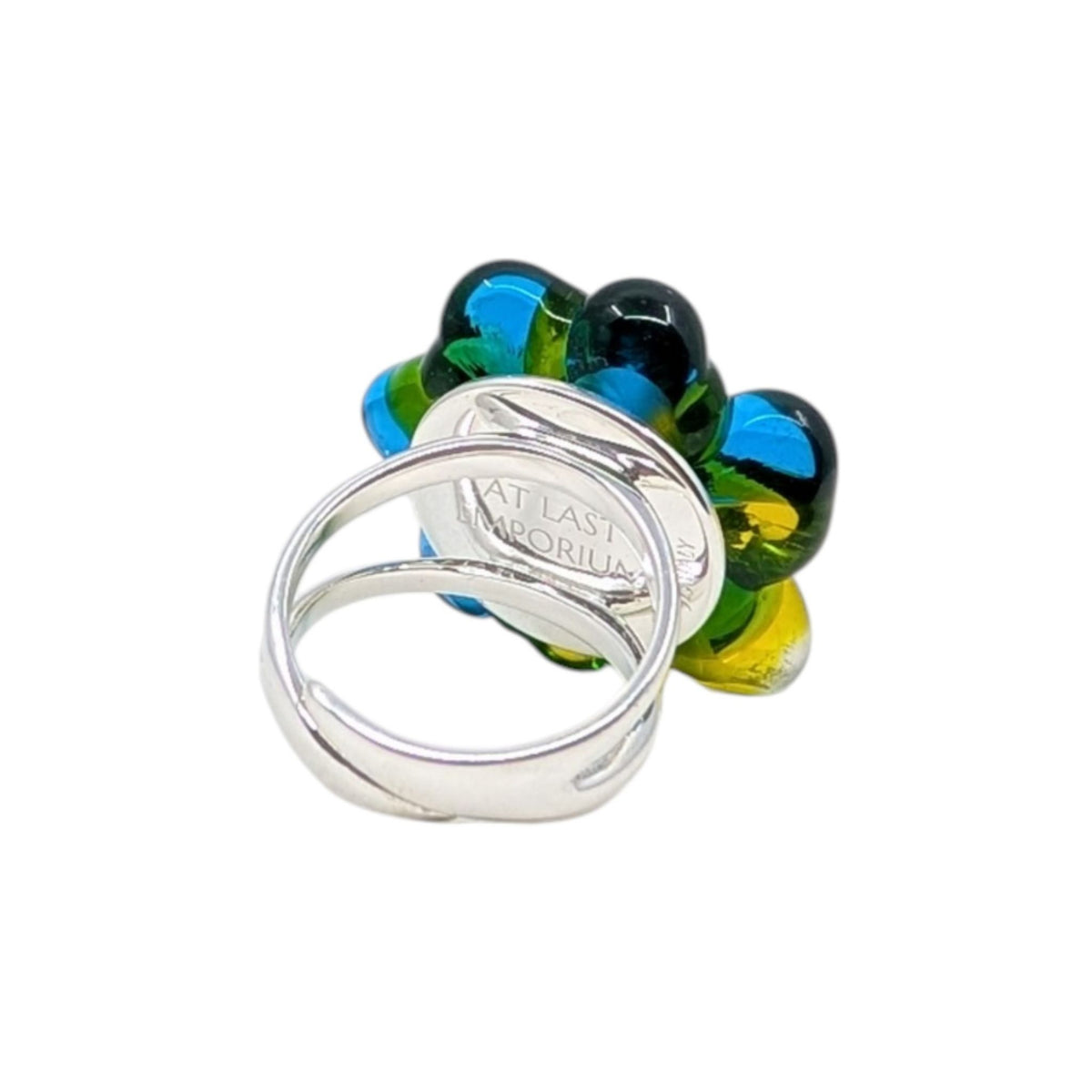 A silver-toned metal ring with a textured band overlapping a flower-shaped ring made of glossy blue and yellow glass, on a plain white background.