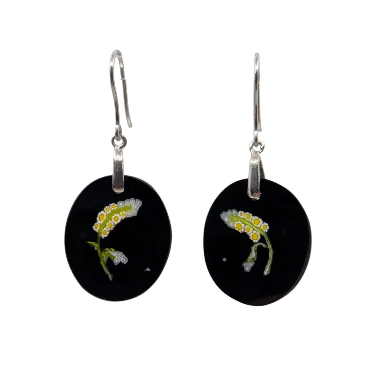 A pair of black oval drop earrings with silver fishhook wires, featuring a small glass white, yellow, and green flower on each earring.