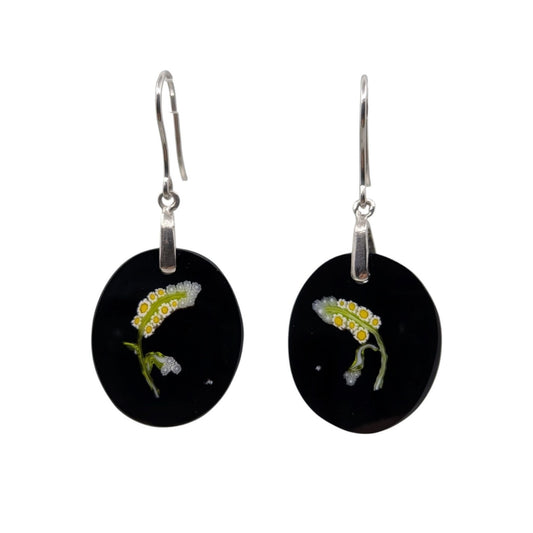 A pair of black oval drop earrings with silver fishhook wires, featuring a small glass white, yellow, and green flower on each earring.