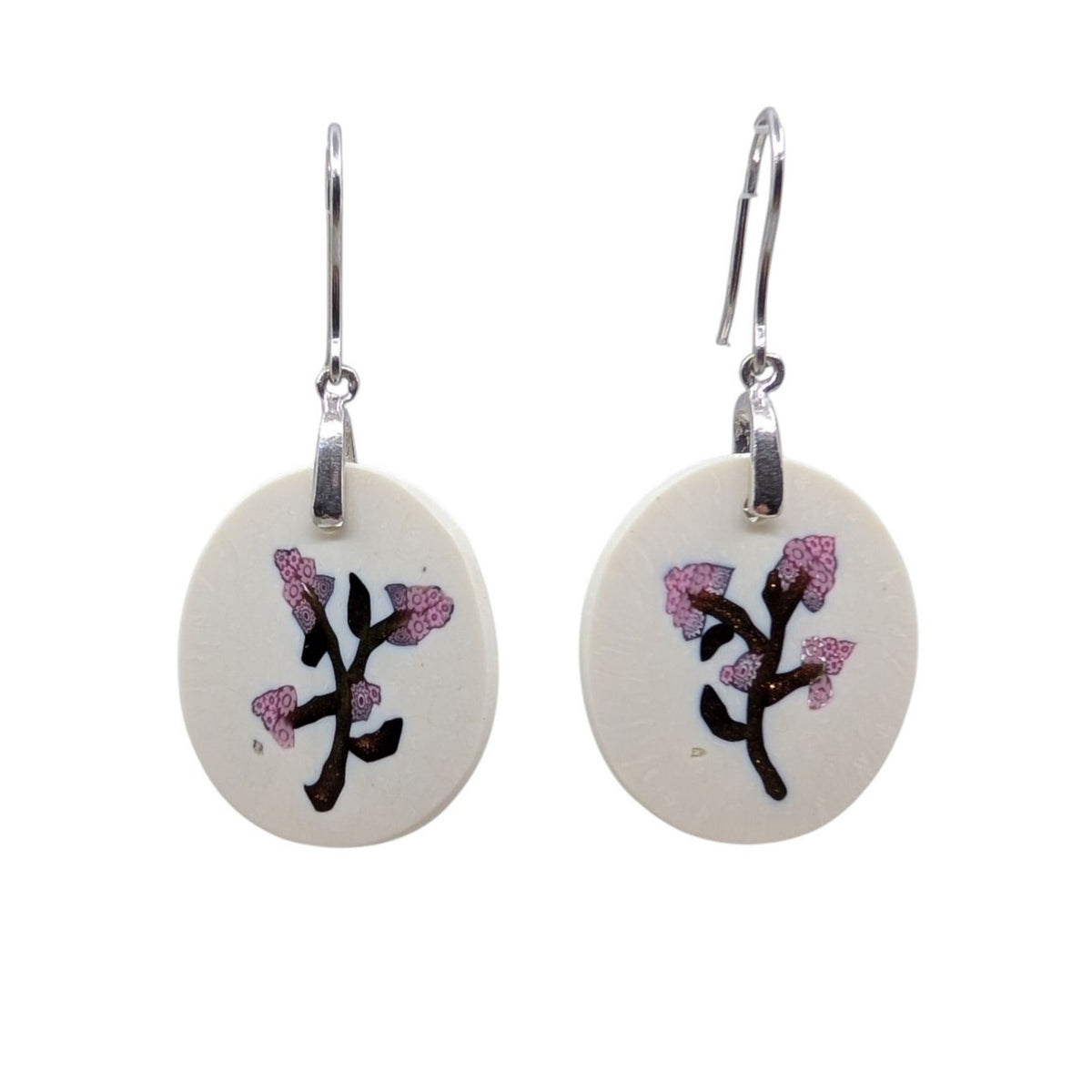 A pair of silver drop earrings with oval cream-colored earrings featuring millefiori  with pink blossoms, shown against a plain white background.