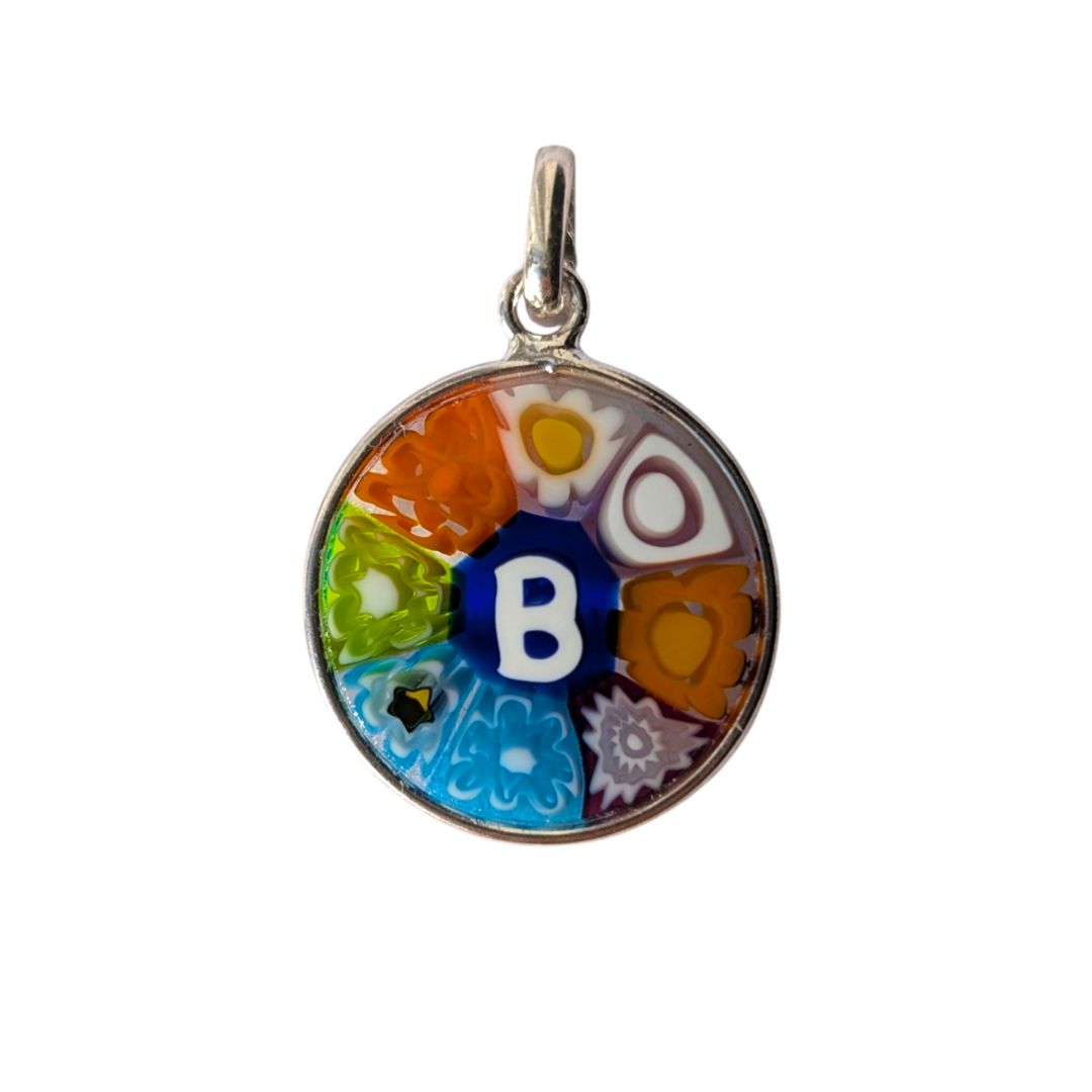A round silver pendant charm featuring a colorful Millefiori-style design with a central white letter 'B' on a blue background, surrounded by orange, green, and light blue floral segments.