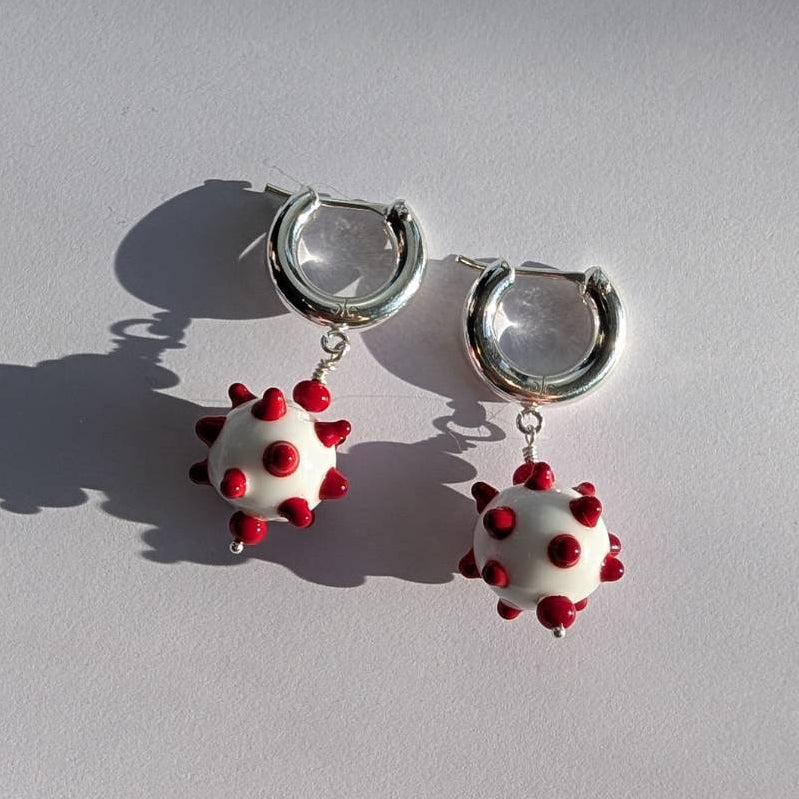 Hoop earrings with white and red spherical charms on a light gray background