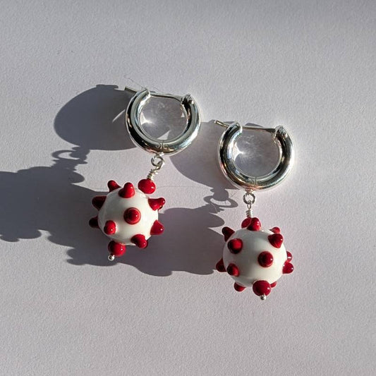 Hoop earrings with white and red spherical charms on a light gray background