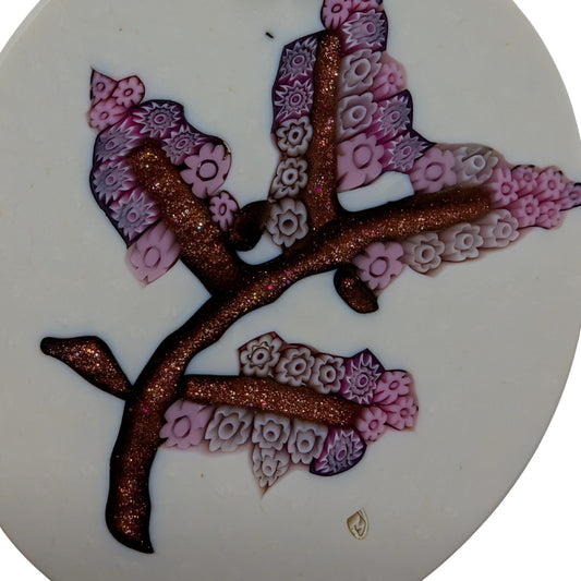 A close-up of a circular white millefiori pendant with a gold branch design with pink and purple floral patterns and glittery  branches.