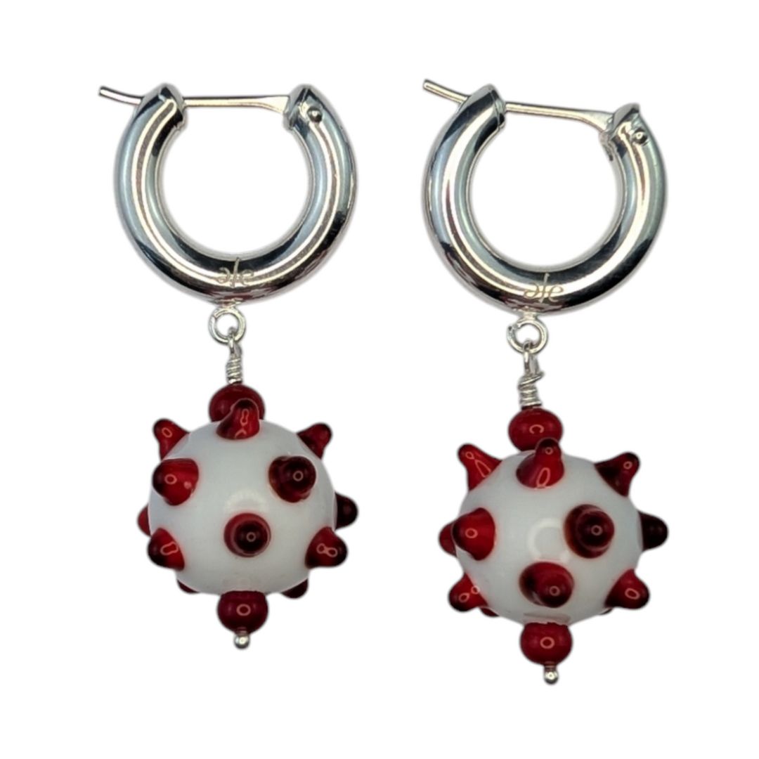 A pair of earrings featuring white and red handmade glass beads with a geometric pattern, attached to lightweight silver hoop earrings.